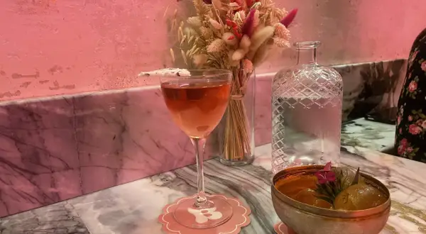 Un cocktail rose et un bol de fruits sur un marbre rose, ambiance douce et romantique d'un bisou bar.
