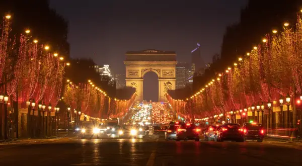 Les Champs-Élysées illuminés pour le réveillon de Noël, avec le trafic parisien et l'Arc de Triomphe en fond.