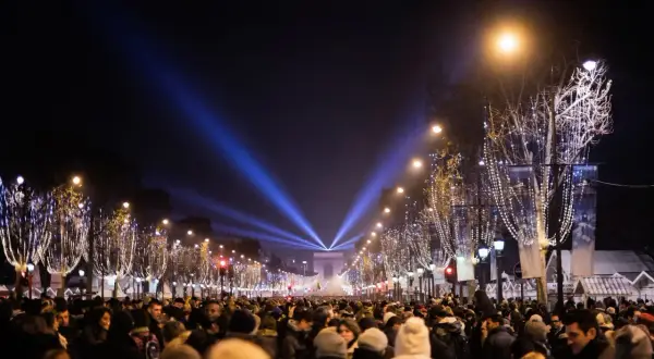 Une foule nombreuse célèbre une **soirée paris** sous les lumières bleues illuminant l'Arc de Triomphe et les arbres décorés de guirlandes.