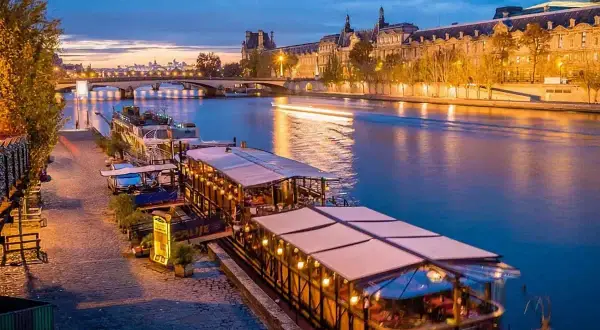 Un restaurant sur Seine à Paris, illuminé et accueillant, reflète ses lumières sur l'eau paisible.