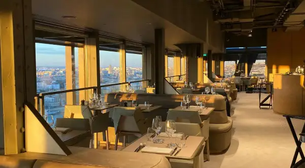 Intérieur d'une brasserie chic avec vue panoramique sur Paris. Les tables sont dressées, prêtes à accueillir les clients pour un dîner inoubliable à la Madame Brasserie Tour Eiffel.