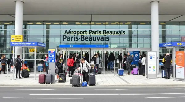 Voyageurs avec bagages devant l'aéroport Paris-Beauvais, prêts pour leur vol.