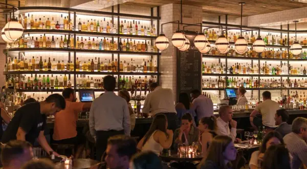 Ambiance chaleureuse dans ce bar gay, avec des étagères remplies de bouteilles et des clients attablés.