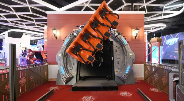 Attraction de manège orange suspendue, prête à faire décoller les visiteurs. Le sol rouge est décoré de motifs "La tête dans les nuages".