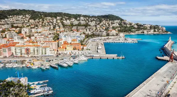 Vue panoramique du port de Nice, avec des yachts amarrés et des bâtiments colorés. On imagine un repas chez Juliette, menu ensoleillé.