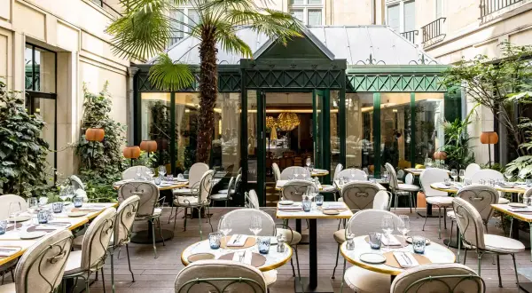 Cour intérieure d'un restaurant chic, tables dressées sous un palmier, ambiance paisible, comme un blossom de sérénité.