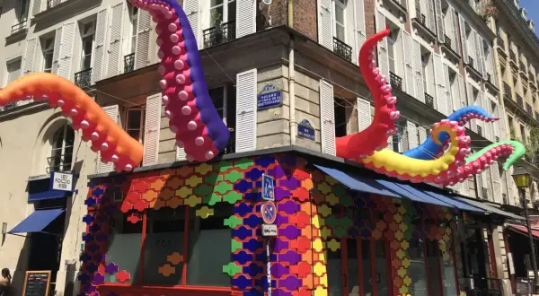 Tentacules colorés géants sortent d'un bâtiment orné de motifs arc-en-ciel, un décor festif pour ce bar gay à Paris.