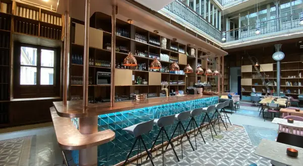 Le bar moderne du "Le Shack Paris" avec son comptoir en cuivre et ses tabourets gris, baigné de lumière naturelle.