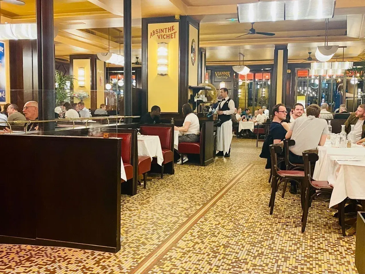 Ambiance chaleureuse dans un bouillon République, avec ses banquettes rouges, ses tables dressées et ses clients attablés.