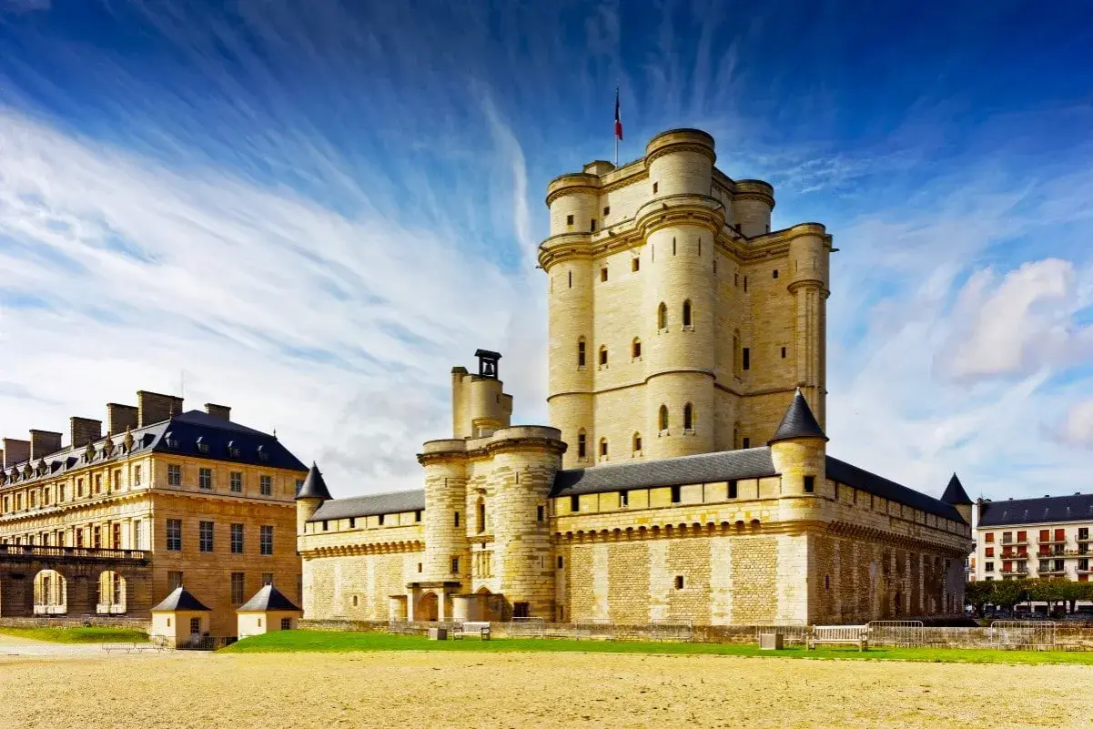 Le majestueux **Château de Vincennes** se dresse sous un ciel bleu éclatant, ses tours imposantes rappelant des siècles d'histoire.