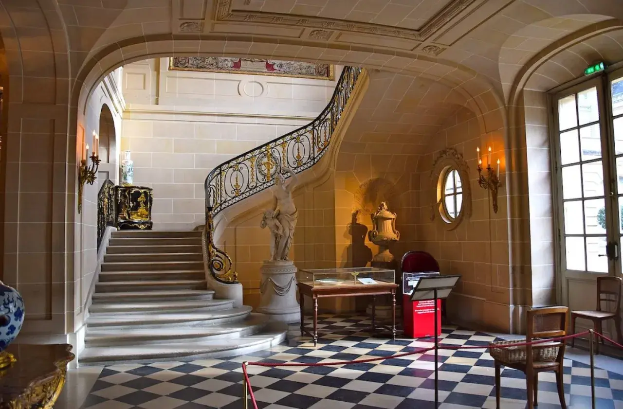 Escalier majestueux du musée Nissim de Camondo, avec sa rampe dorée, sa statue et son sol à damier.