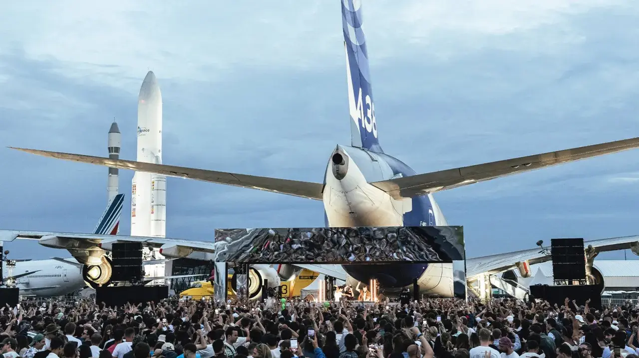 Foule immense devant une scène, sous des avions et des fusées. Ambiance de festival Cercle.