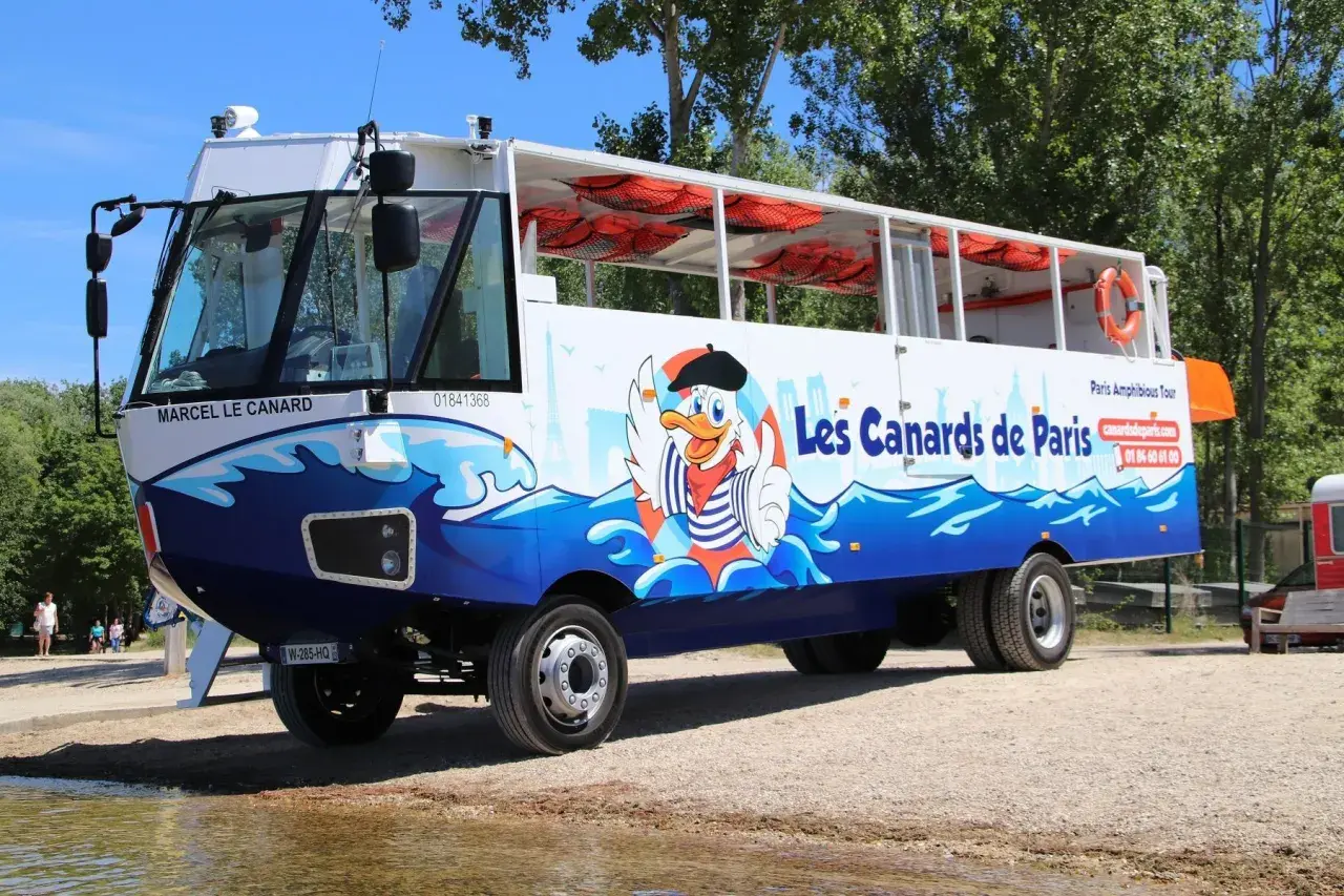Un bus amphibie décoré de "Les Canards de Paris" avec un canard cartoon, prêt pour une aventure sur l'eau et la terre.