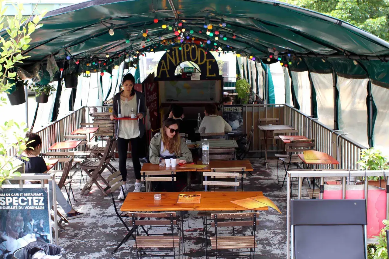 Terrasse animée d'un café-restaurant sur une péniche à Paris, avec des tables en bois, des lumières colorées et des plantes.