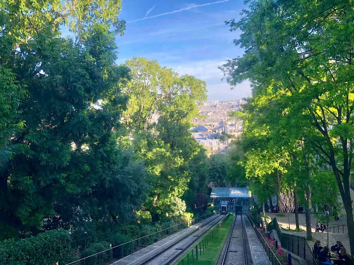 Vue sur le funiculaire de Montmartre, avec Paris en arrière-plan. Les arbres verdoyants encadrent la scène.