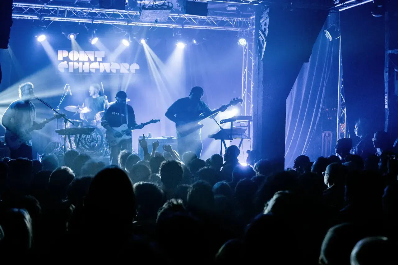 Un groupe joue sur scène sous des lumières bleues. Découvrez les **upcoming concerts in Paris** !