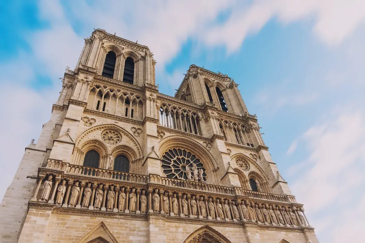 Notre Dame de Paris, une visite inoubliable. La façade majestueuse de la cathédrale se dresse sous un ciel bleu et nuageux.