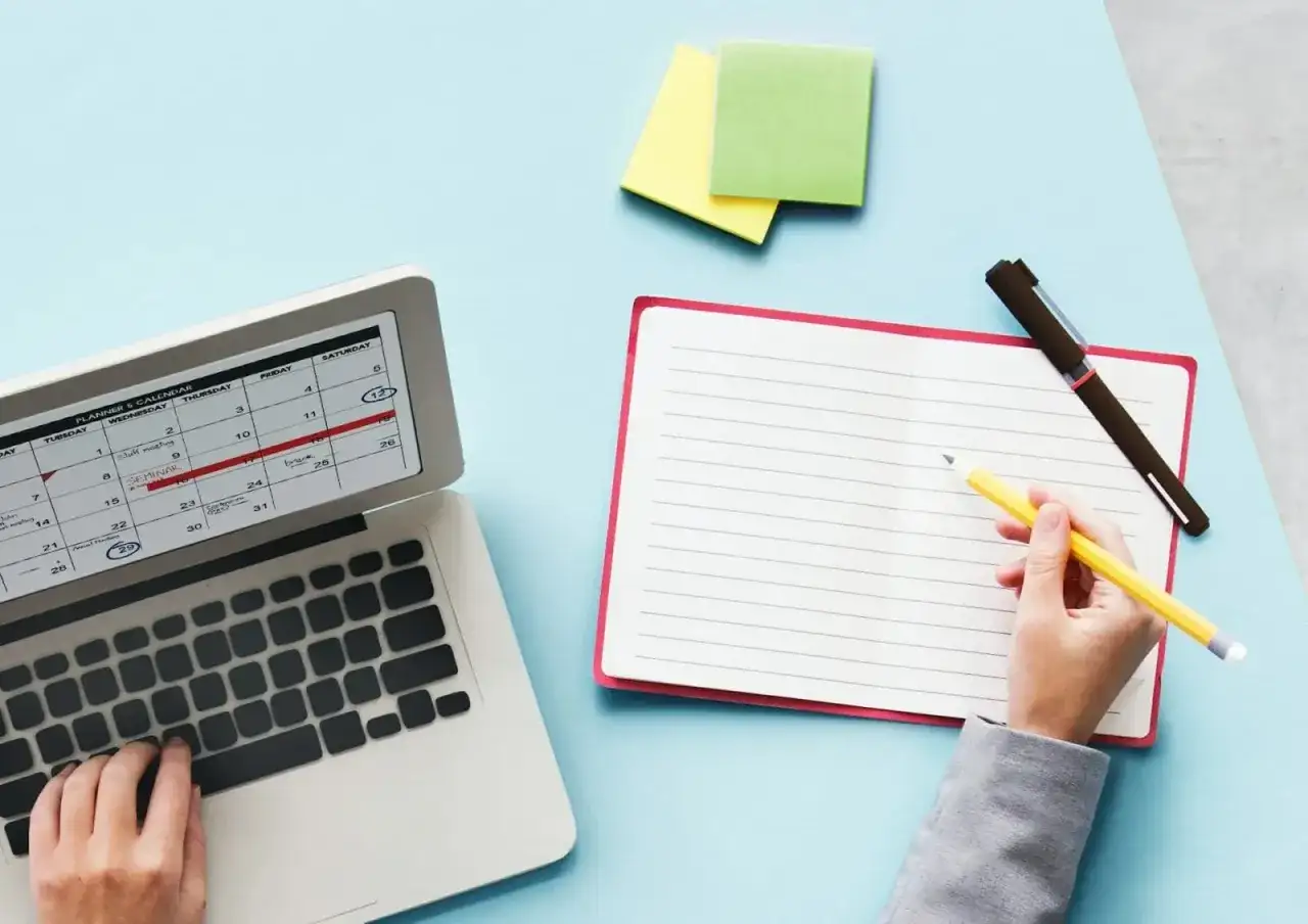 Planification des jours fériés 2026 sur un calendrier d'ordinateur. Une main écrit dans un carnet à côté.