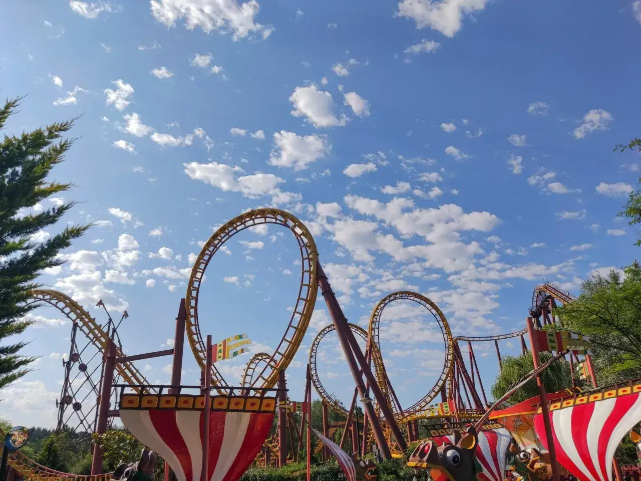 Montagnes russes jaunes et rouges dans un parc attraction, sous un ciel bleu parsem&eacute; de nuages blancs.