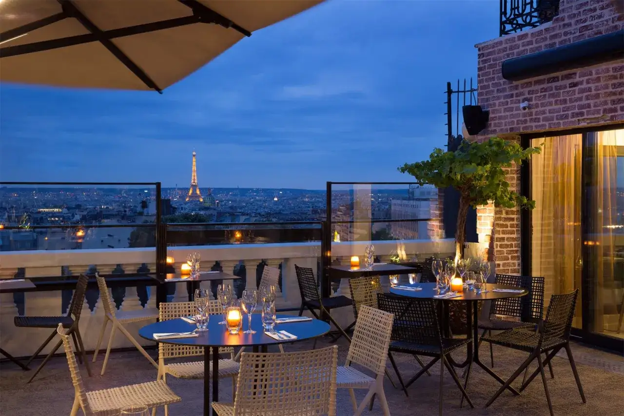 Terrasse d'un restaurant parisien avec vue sur la Tour Eiffel illumin&eacute;e. Tables dress&eacute;es pour un d&icirc;ner romantique, ambiance 