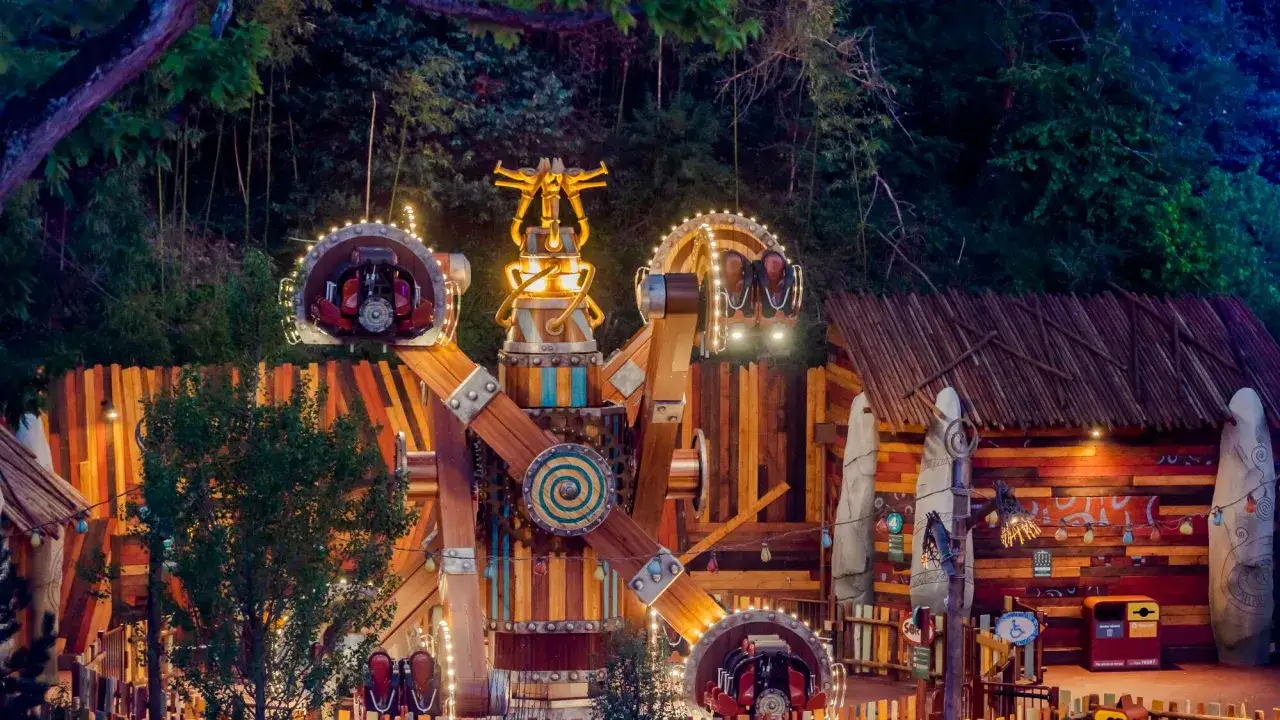 Attraction du Parc Astérix illuminée la nuit, avec ses nacelles en rotation et sa structure en bois.