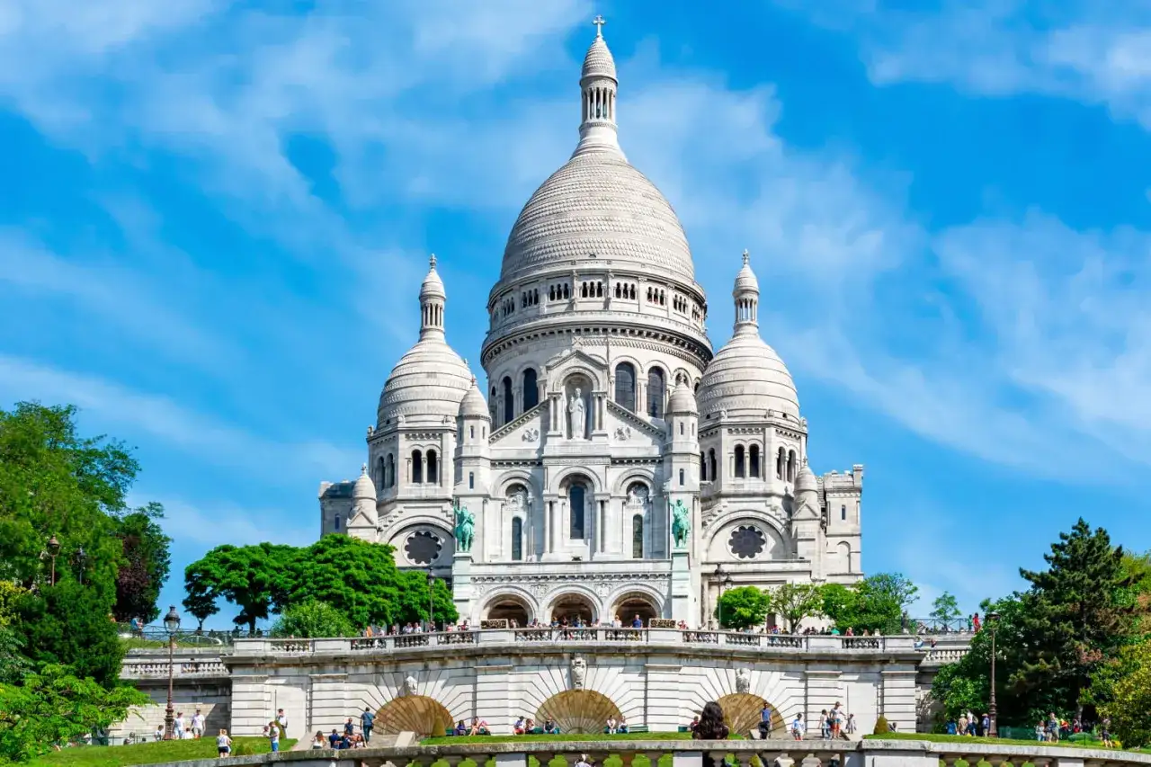 La basilique du Sacré-Cœur domine Paris, accessible par le funiculaire de Montmartre. Des visiteurs profitent du soleil sur les marches.