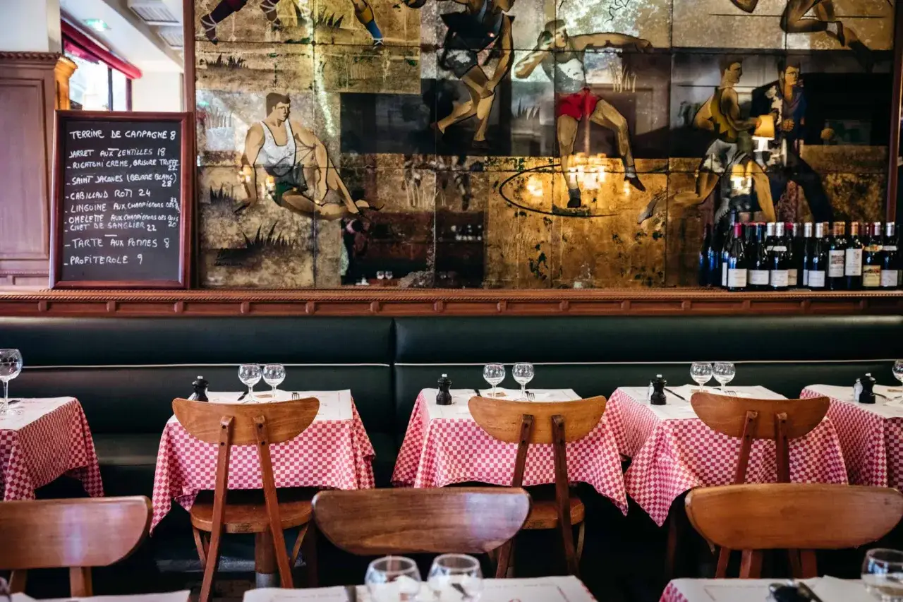 Ambiance chaleureuse d'un meilleur bistrot parisien avec ses tables dress&eacute;es, ses banquettes en cuir et sa fresque murale vintage.