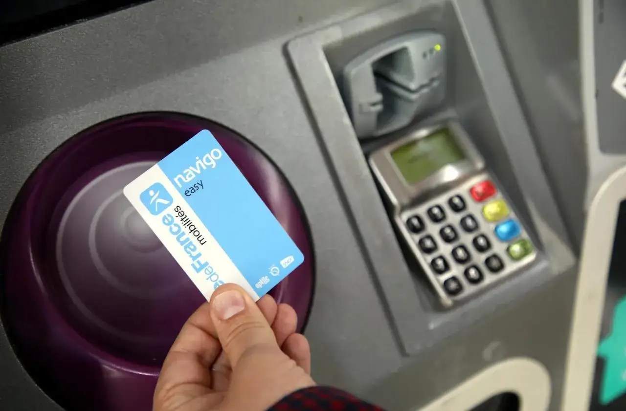 Main d'une personne tenant une carte Navigo Easy, un titre de transport pour le m&eacute;tro parisien, pr&egrave;s d'une borne.