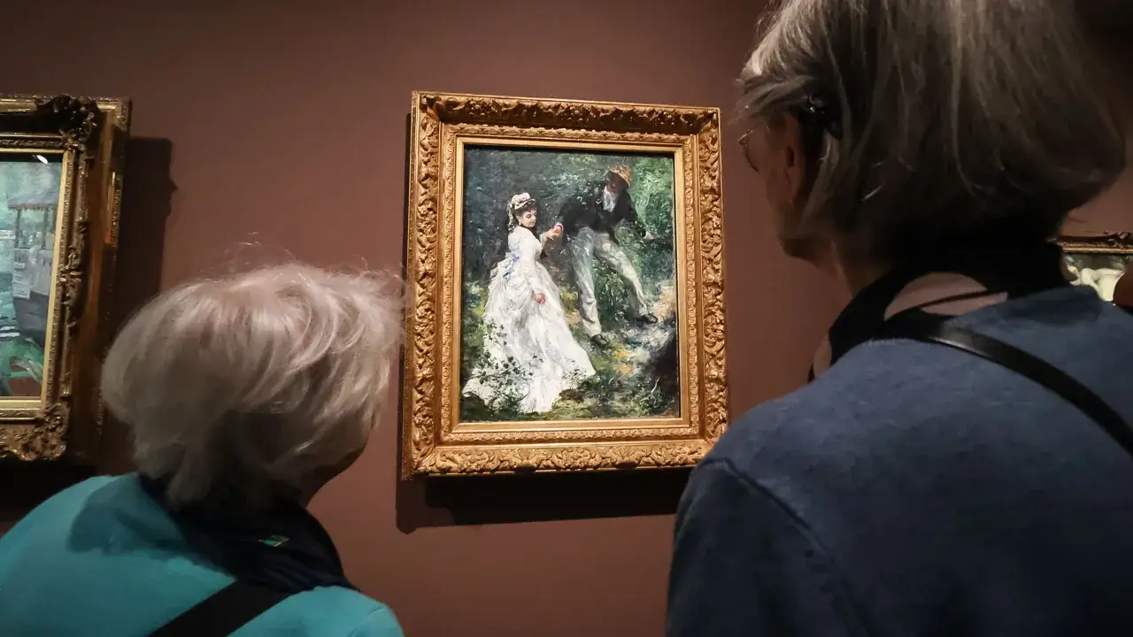 Deux personnes admirent une peinture de Renoir repr&eacute;sentant un couple dans un jardin.
