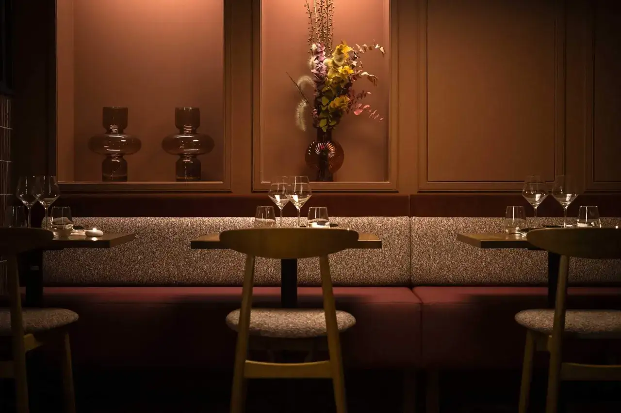 Ambiance feutrée d'un restaurant incontournable à Paris. Tables dressées, banquettes confortables, vases décoratifs et bouquet de fleurs séchées.