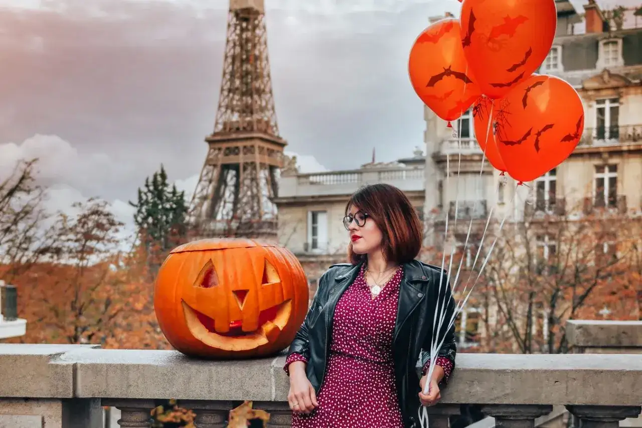 Une femme avec des ballons orange et une citrouille sculpt&eacute;e, devant la Tour Eiffel. Id&eacute;e de quoi faire pour Halloween &agrave; Paris.