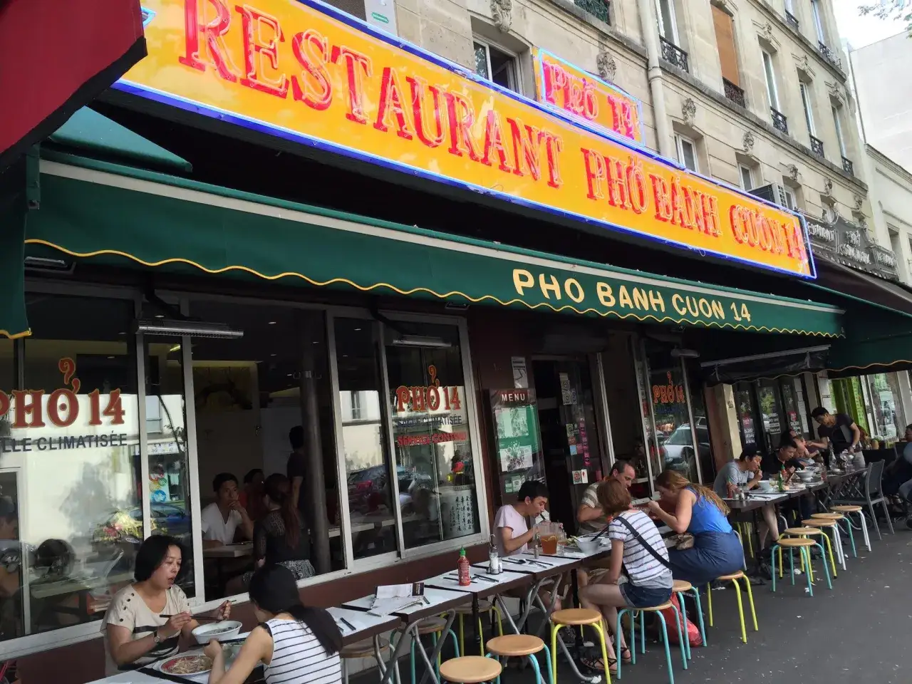Restaurant Pho 14, une enseigne lumineuse promet le meilleur pho. Des clients savourent ce plat r&eacute;confortant en terrasse.