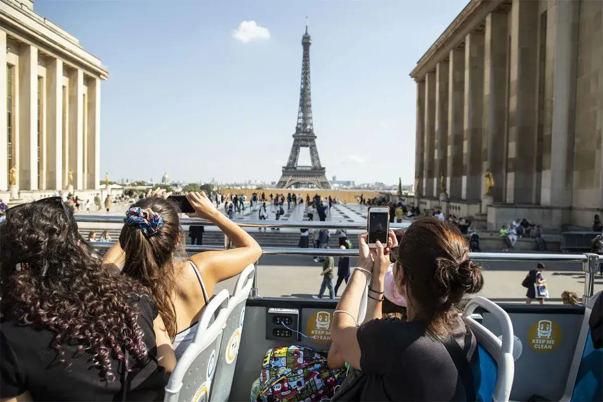 Vue de la Tour Eiffel depuis un bus hop on hop off Paris. Des touristes prennent des photos.