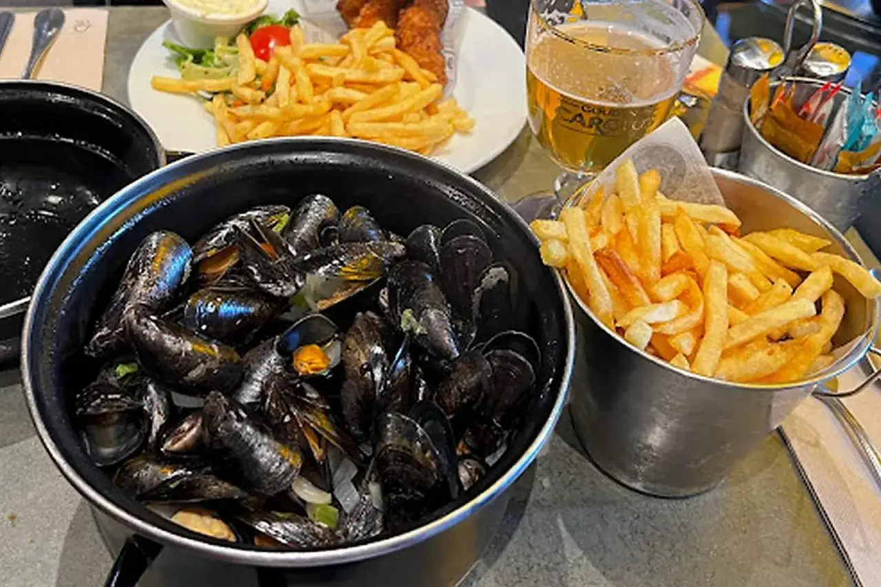 Un plat de moules marinières fumantes avec des frites croustillantes, un verre de bière et une salade. Le meilleur moules frites Paris, un délice !