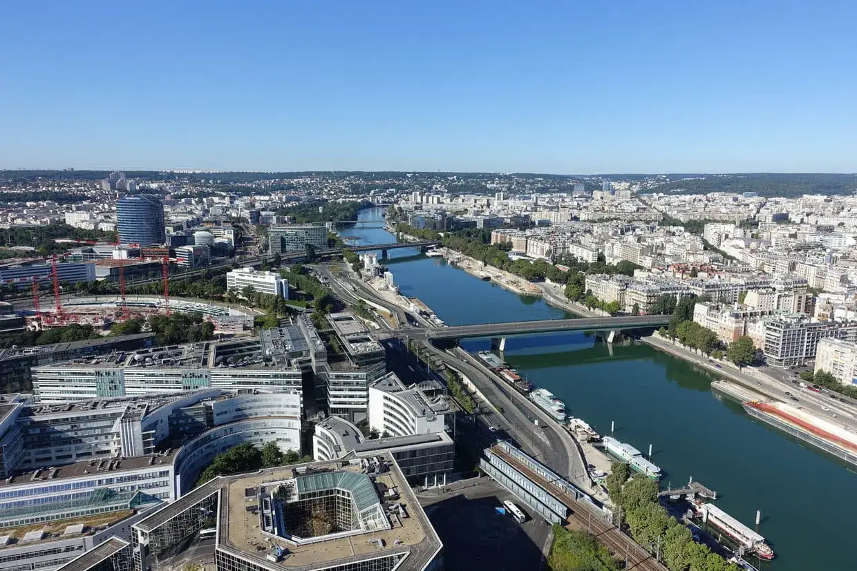 Vue aérienne de Paris, le long de la Seine. Un ballon dirigeable survole la ville, offrant une perspective unique sur les ponts et les bâtiments modernes.