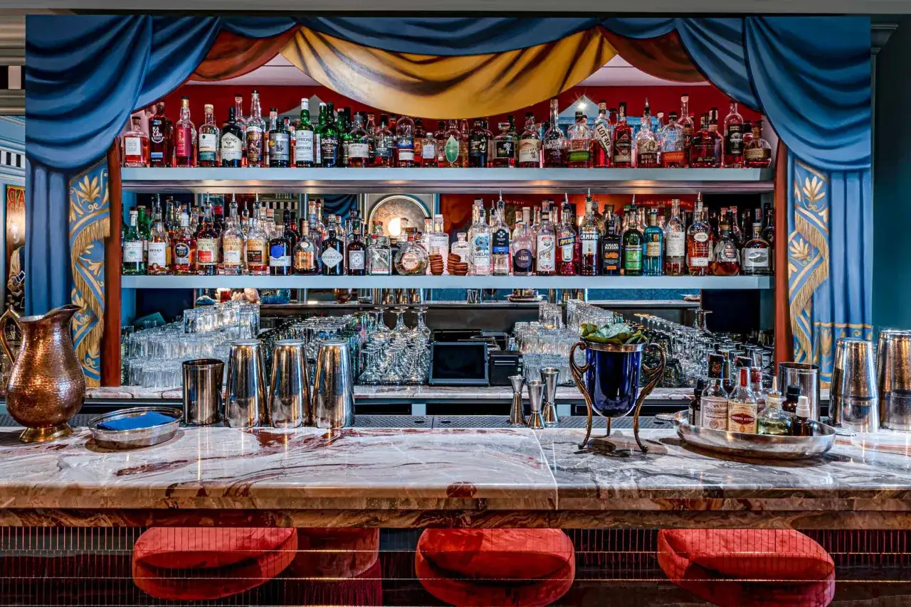 &Eacute;tag&egrave;res remplies de bouteilles d'alcool, un bar en marbre avec des tabourets rouges, pr&ecirc;t pour un baby bar.