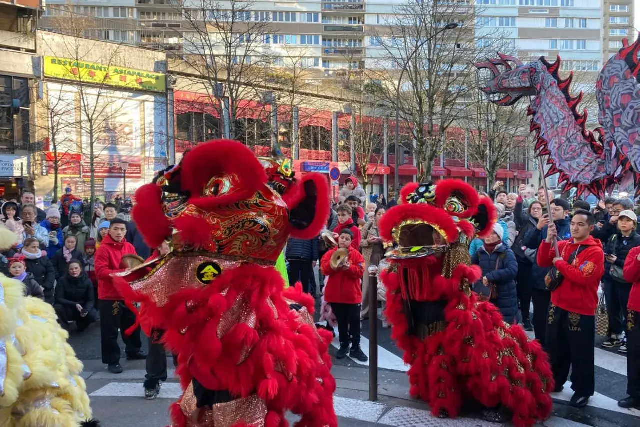 Danse des lions rouges et d'un dragon lors d'un d&eacute;fil&eacute; du nouvel an chinois, sous les regards d'une foule joyeuse.