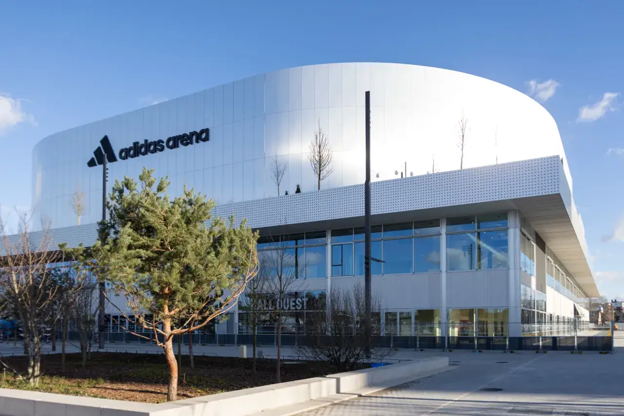 La moderne adidas arena Paris, avec son logo embl&eacute;matique, se dresse sous un ciel bleu. Des arbres verdoyants bordent l'entr&eacute;e.