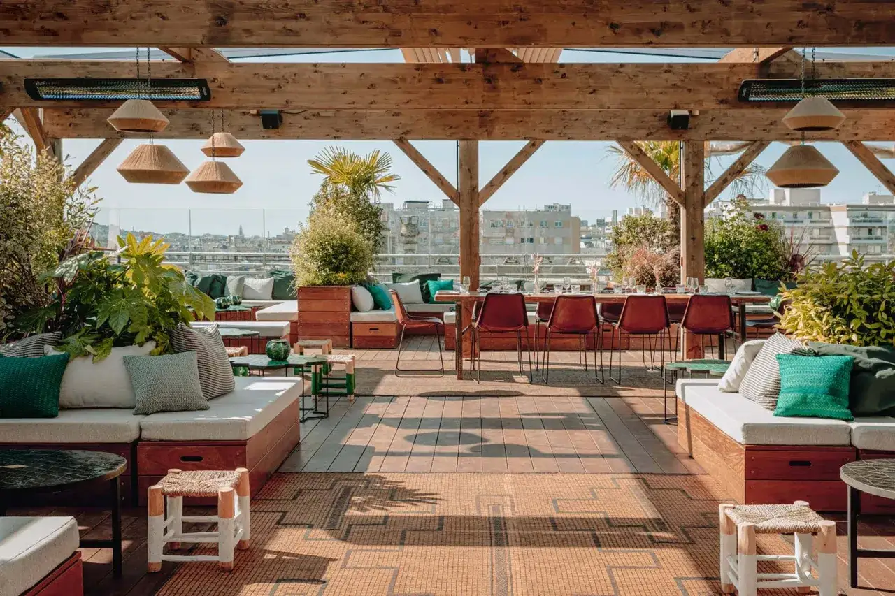 Le perchoir M&eacute;nilmontant : un rooftop chic avec vue sur Paris, mobilier confortable, verdure luxuriante et tables dress&eacute;es pour un moment suspendu.