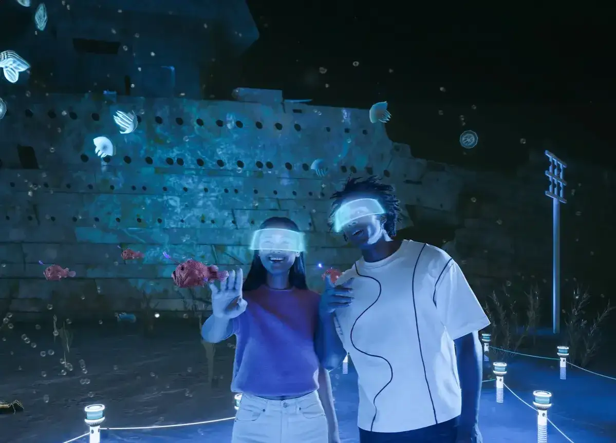 Deux jeunes explorent un monde sous-marin en réalité virtuelle à Paris La Villette, interagissant avec des poissons et des méduses devant une épave.