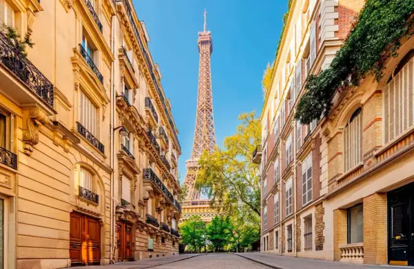 Vue sur la Tour Eiffel entre deux immeubles parisiens, un jour férié de mai. Les balcons ornés et les façades en pierre rappellent le charme de la capitale.