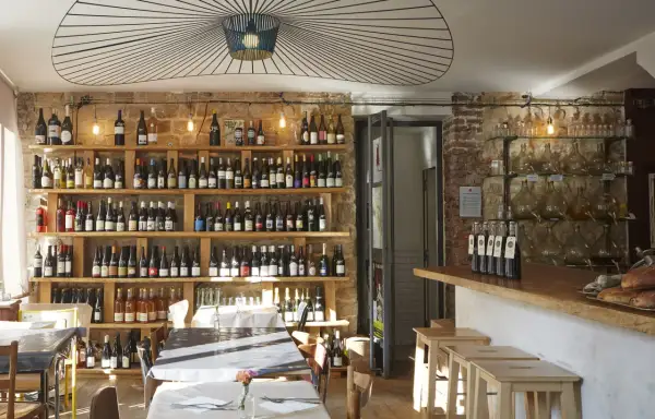 Ambiance chaleureuse dans la cave à manger, avec des étagères remplies de bouteilles de vin, des tables dressées et un bar en bois.
