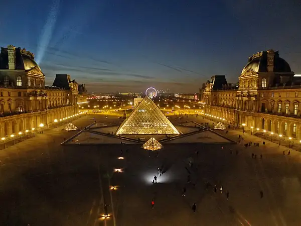 La Pyramide du Louvre illuminée, une belle soirée du 14 juillet. La foule admire le spectacle nocturne.