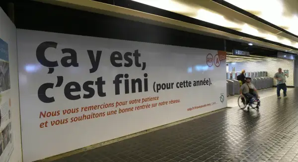 Panneau RATP annonçant la fin des travaux sur le RER A. Une personne en fauteuil roulant passe devant.