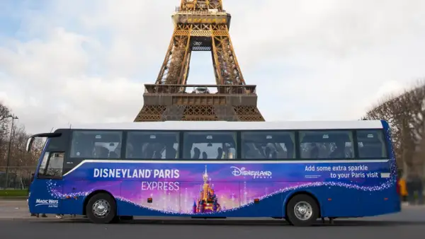 Un bus Disneyland Paris Express, décoré d'un château féerique, passe devant la Tour Eiffel.