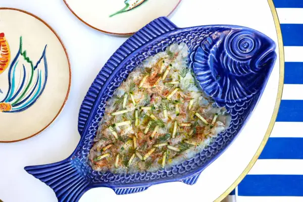 Un délicieux carpaccio de poisson servi dans un plat bleu en forme de poisson, parfait pour un déjeuner à Paris.