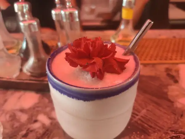 Un cocktail crémeux orné d'une fleur rouge, prêt à être dégusté. Un vrai "menu de bar-bisou" pour une soirée douce.