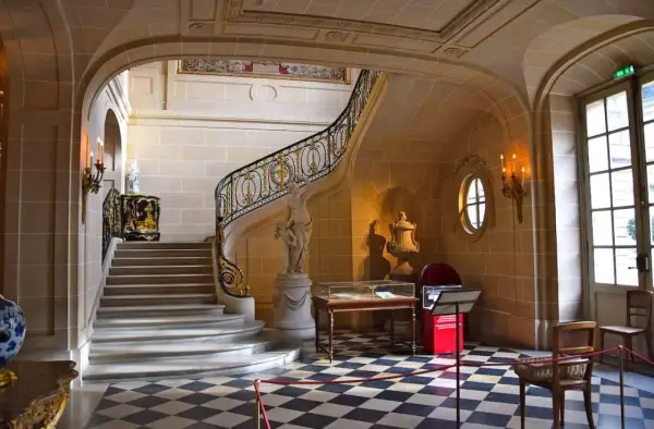 Escalier majestueux du musée Nissim de Camondo, avec sa rampe dorée, sa statue et son sol à damier.