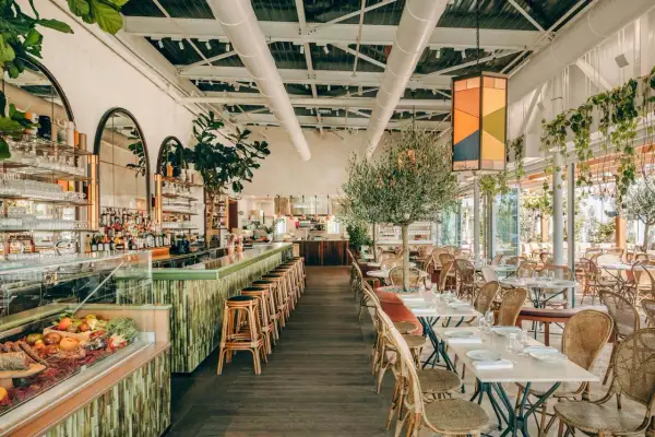 Ambiance chic au Perchoir Porte de Versailles : bar animé, tables dressées, oliviers et végétation luxuriante pour un repas en terrasse.