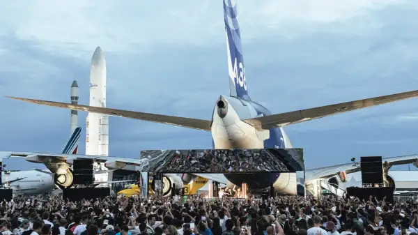 Foule immense devant une scène, sous des avions et des fusées. Ambiance de festival Cercle.